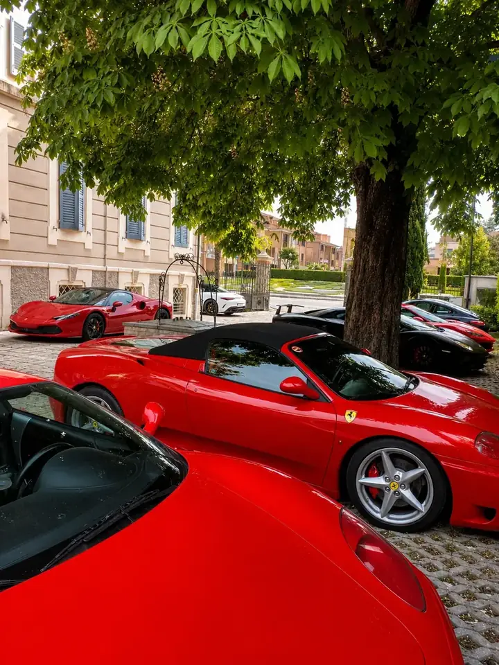 Ferrari rosse parcheggiate all'ombra degli alberi